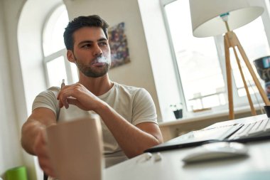 Genç adam iş gününün ortasında sigara içiyor ve kahve içiyor. 
