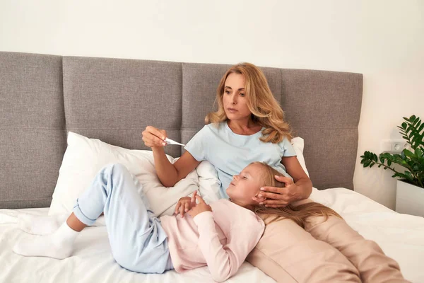 Uma foto de uma mãe verificando a febre de suas filhas com termômetro — Fotografia de Stock