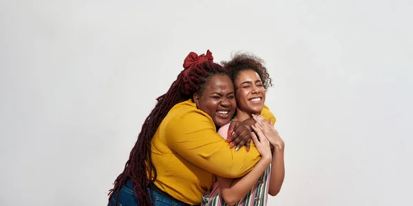 Due donne africane stanno avendo fan sulla macchina fotografica abbracciare e in piedi sopra il muro bianco — Foto Stock