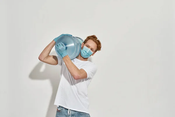 Young, redhead deliveryman holds giant bottle with both hands on his shoulder — Stock Photo, Image