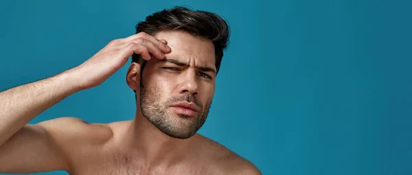 Estúdio retrato de homem sem camisa verificando sua pele, à procura de manchas, posando isolado sobre fundo azul — Fotografia de Stock