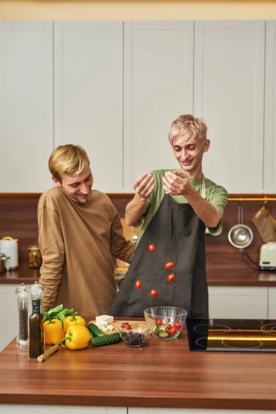 Sonriente pareja gay macho preparando ensalada con tomates —  Fotos de Stock