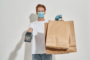 Genç kızıl saçlı teslimatçı önünde kese kağıdı ve terminal tutuyor.