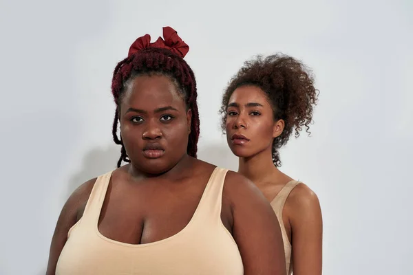 Portrait of african american women in underwear with different body size looking at camera, standing together isolated over gray background — Stock Photo, Image