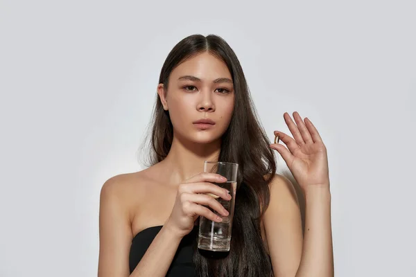 Νεαρή Ασιάτισσα που κρατάει χάπια και ένα ποτήρι νερό — Φωτογραφία Αρχείου