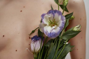 Kadının çıplak göğsünün üzerinde Eustoma çiçekleri taşıdığı yakın çekim.