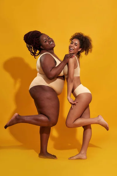 两个穿着不同体形的内裤的漂亮的年轻的非洲裔美国女人在黄色的背景下摆出孤立的姿势 — 图库照片