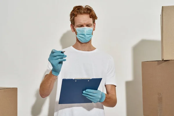 Young courier fills in delivery-details, holding a clipboard and a pen in hands — Stock Photo, Image