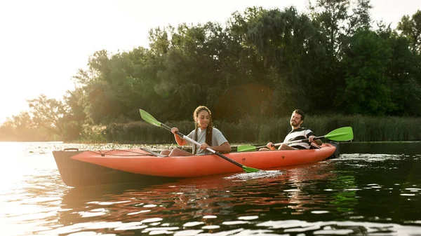 Kalandos fiatal pár kajakozik a folyóban, körülvéve a gyönyörű természettel egy nyári napon. — Stock Fotó