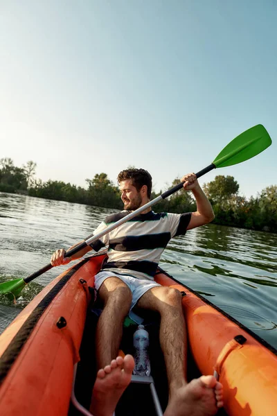 Активный молодой человек с энтузиазмом смотрит во время плавания на байдарках в озере, окруженный мирной природой в летний день — стоковое фото