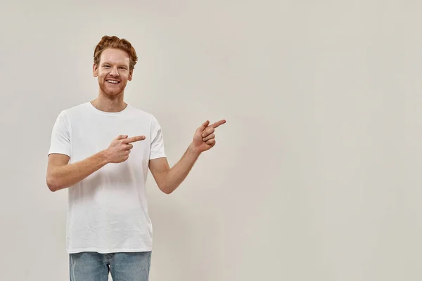 Jonge roodharige staat aan de linkerkant van de foto en wijst naar het tegenovergestelde — Stockfoto