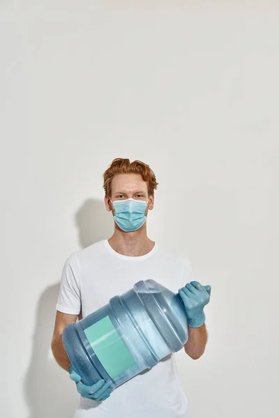 Young redhead deliveryman holds a huge bottle of water with both hands in front of him — Stock Photo, Image