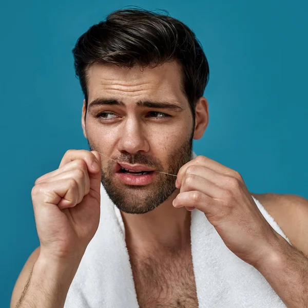 Close-up portret van knappe blanke man het reinigen van gezonde tanden met behulp van tandzijde geïsoleerd over blauwe achtergrond — Stockfoto