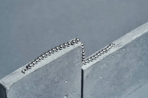회색 배경 위로 분리 된 콘크리트 요소 위에 놓인 은색 공 목걸이의 근접 사진 — 스톡 사진