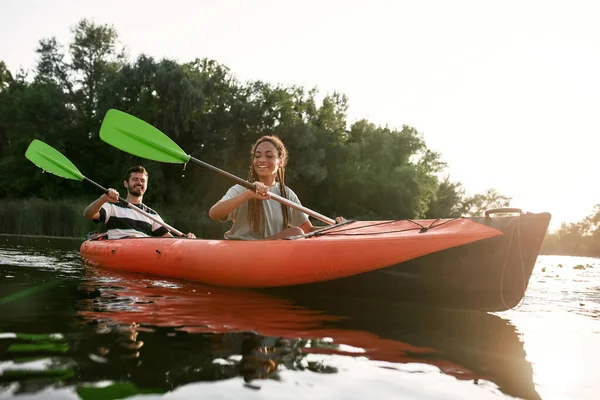 Sorridente giovane donna e il suo ragazzo godendo kayak in un lago in un pomeriggio di fine estate — Foto Stock