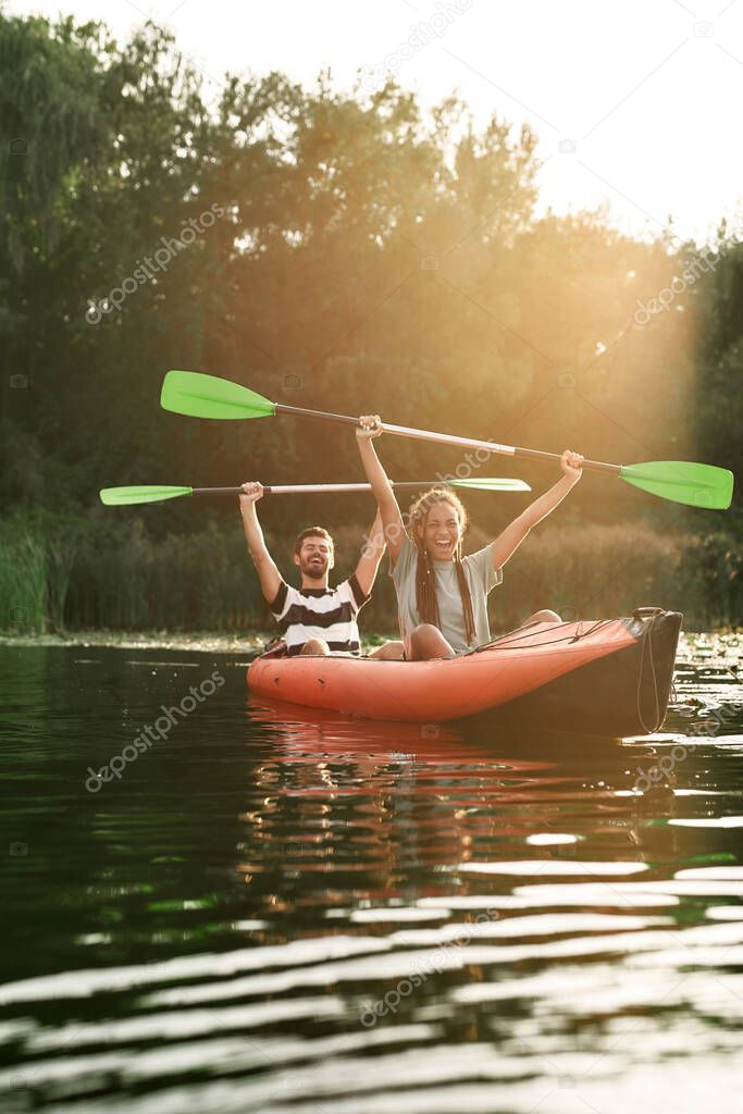 Couple of excited friends having fun while kayaking in a river surrounded by the beautiful nature on a summer day
