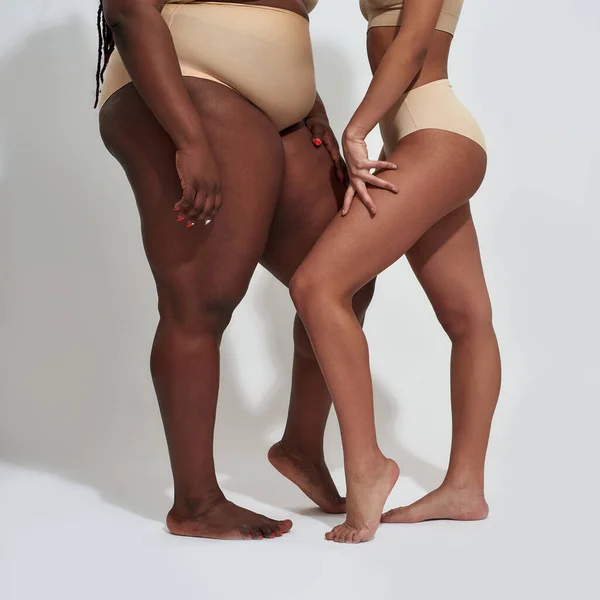 Nogi dwóch kobiet w beżowej bieliźnie o różnej wadze, odizolowanych na szarym tle — Zdjęcie stockowe