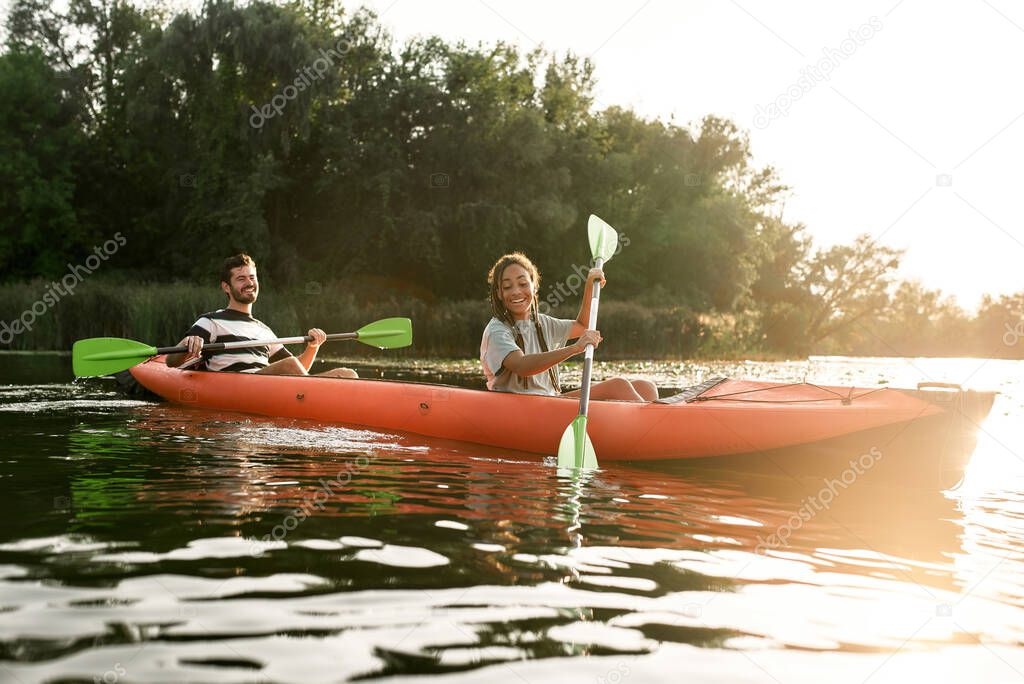 Two adventurous young friends kayaking in a river surrounded by the beautiful nature on a summer day