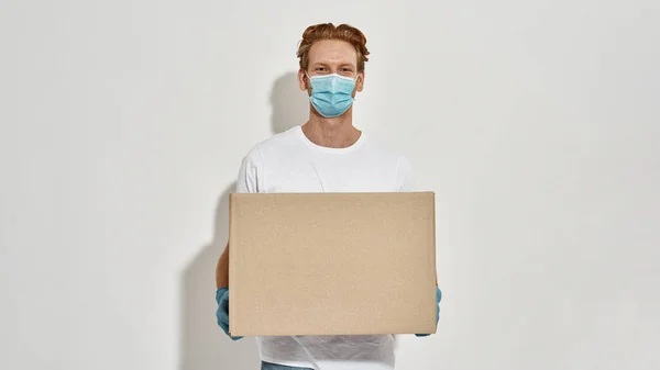 Young delivery boy holds big cardboard box in front of him — Stock Photo, Image
