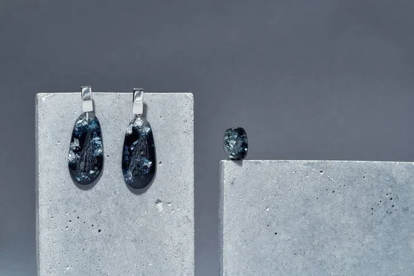 Conjunto artesanal de um anel e pendurar brincos de lágrima feitos de resina epóxi azul escuro com folha de prata no interior em elementos de concreto isolados sobre fundo cinza — Fotografia de Stock