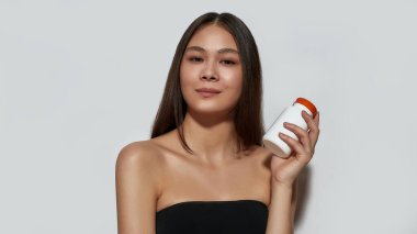 Gülümseyen Asyalı genç kız elinde hap kutusu tutuyor.