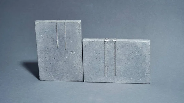 스튜디오는 회색 배경에 분리 된 콘크리트 요소 위에 2 쌍의 스테일 링은 장신구를 매달아 놓은 사진을 촬영했다. — 스톡 사진