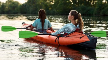İki genç kadının güzel doğayla çevrili bir gölde birlikte tekneye binişlerinin arka görüntüsü.