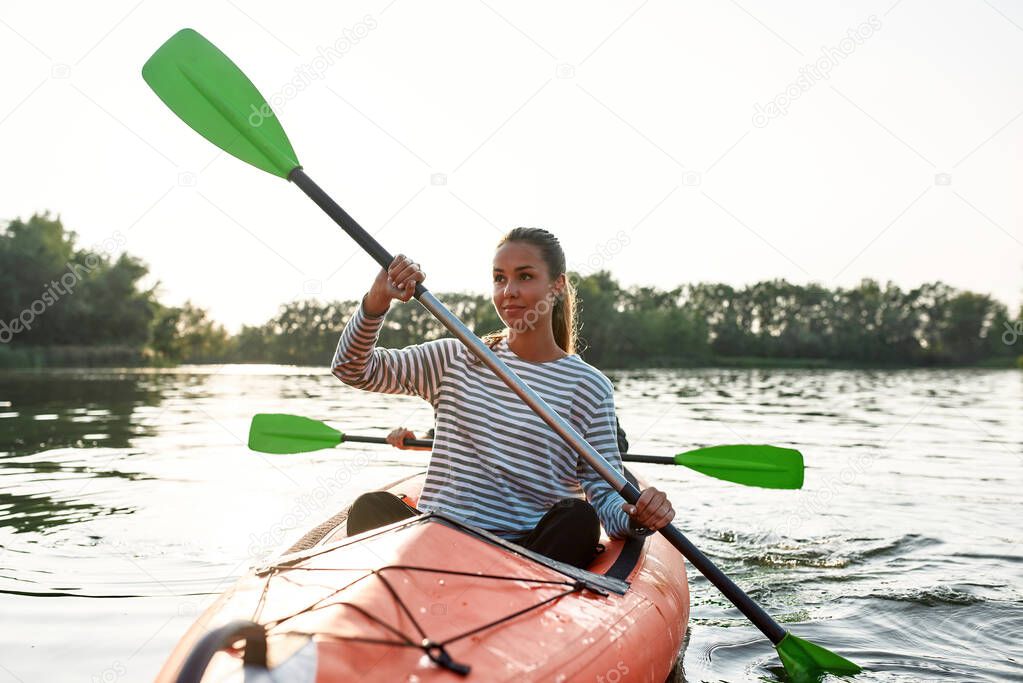 Attractive young woman smiling away, walking by kayak together with her boyfriend on a summer day