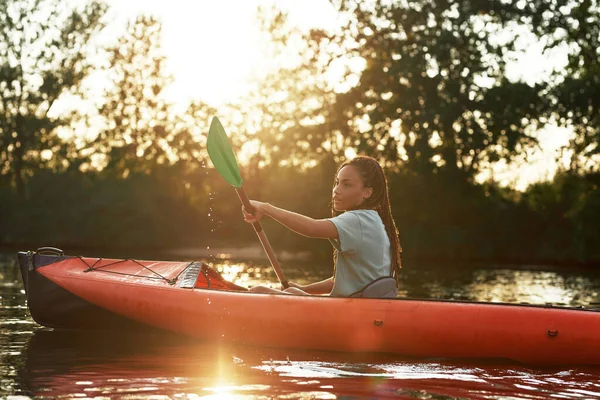 Aantrekkelijke jonge vrouw die een peddel vasthoudt terwijl ze kajakt in een meer midden in de natuur op een late zomermiddag — Stockfoto