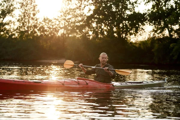 Young caucasian guy paddling kayak on a lake surrounded by peaceful nature at sunset — Stock Photo, Image