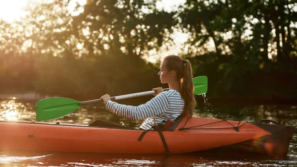 Giovane donna caucasica che regge una pagaia mentre fa kayak in un lago immerso nella natura in un pomeriggio di fine estate — Foto Stock