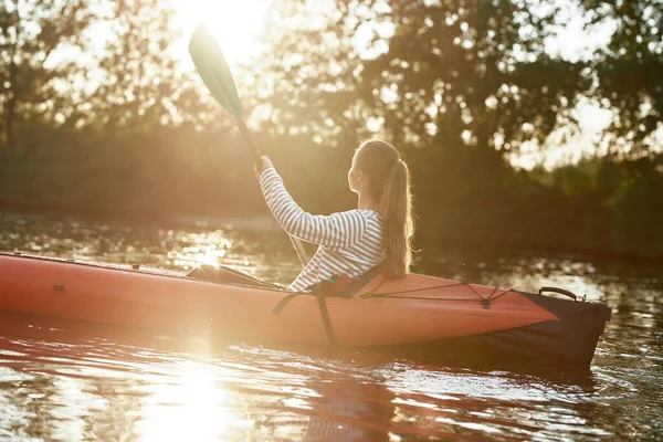 Kaukasische junge Frau sieht entspannt aus, hält ein Paddel in der Hand und paddelt an einem Spätsommernachmittag in einem See inmitten der Natur — Stockfoto