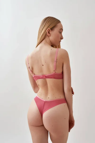 Vista posterior de la mujer caucásica joven en forma con ropa interior transparente rosa de pie, posando aislado sobre fondo gris claro —  Fotos de Stock