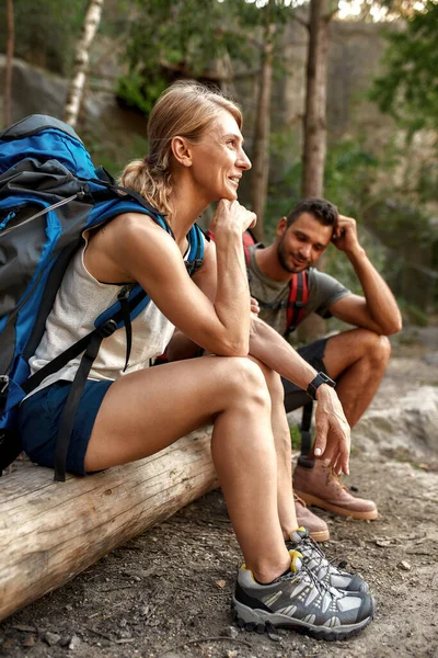 Lächelnde junge kaukasische Touristen sitzen auf Baumstämmen — Stockfoto