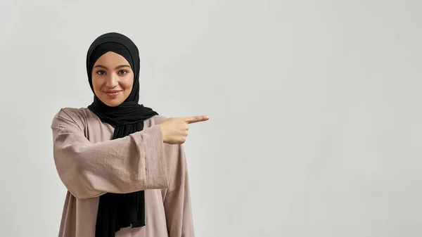 Усміхнена молода арабська жінка в хіджабі вказує на бік — стокове фото