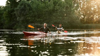 Two male friends looking cheerful while boating together on a lake surrounded by peaceful nature
