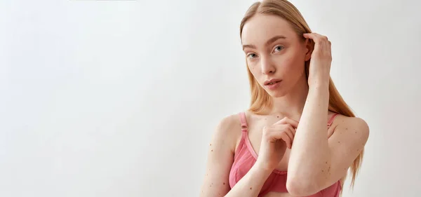 性感的年轻高加索女模特儿穿着粉色透明胸罩看着相机，调整头发，同时在浅灰背景下保持独立的肖像 — 图库照片