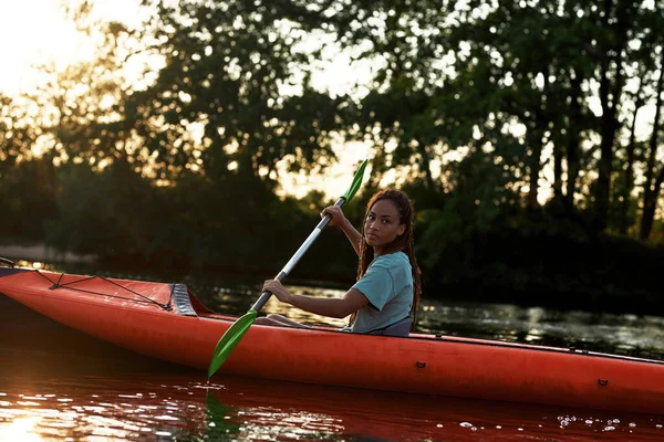 Relaxed young woman looking aside while paddling kayak on a lake surrounded by nature — Stockfoto