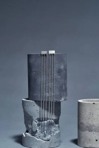 세련 된 미니멀리즘인 스테일 링은 회색 바탕에 분리 된 둥근 콘크리트 요소에 체인 귀걸이를 달고 있다 — 스톡 사진