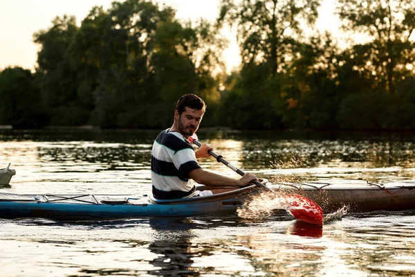 Enthusiastic young caucasian guy having fun while boating on a lake surrounded by nature — Stockfoto