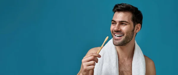 Beauty portrait of cheerful bearded man with towel around neck smiling away with toothpaste in his mouth while brushing teeth isolated over blue background — Zdjęcie stockowe
