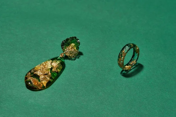 Stylish set of handmade ring and dangle earring made of epoxy resin with golden foil inside isolated over green background —  Fotos de Stock