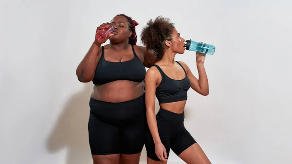 Couple of afro women drinking from sport-bottles, self acceptance concept — Foto de Stock