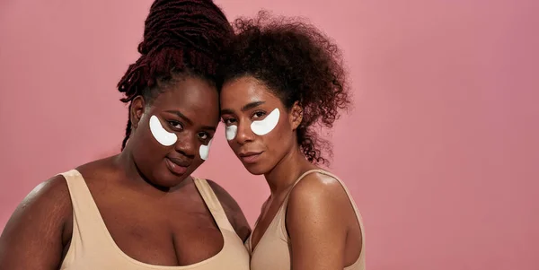 Couple of african women wearing white patches and standing over the pink wall, watching in camera — Stock Photo, Image