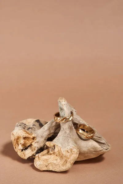 Dos elegantes anillos de oro con muescas dispuestas en elemento de madera sobre fondo beige —  Fotos de Stock