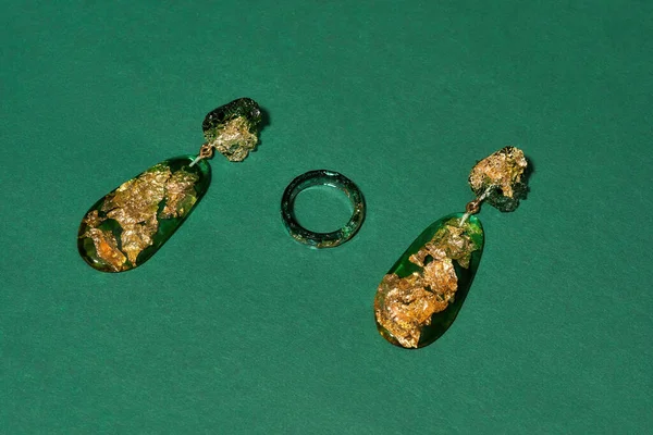 Elegante conjunto de anillos hechos a mano y pendientes colgantes de resina epoxi con lámina dorada en el interior aislada sobre fondo verde —  Fotos de Stock