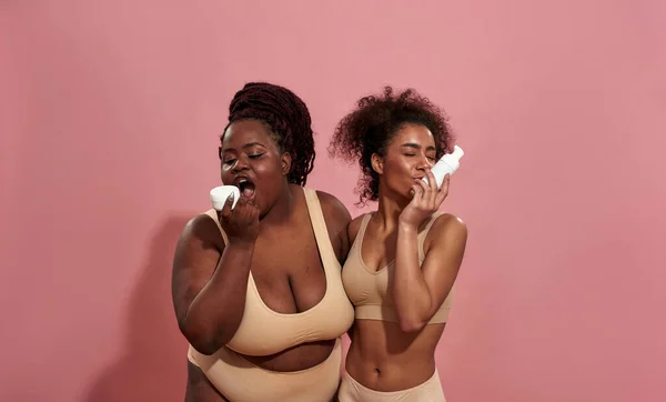 Pareja de mujeres afro en tops beige jugando con productos para el cuidado — Foto de Stock