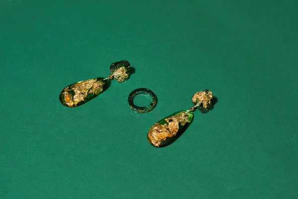 Handgemachtes Set aus einem Ring und Ohrhängern aus Epoxidharz mit goldener Folie innen isoliert über grünem Hintergrund — Stockfoto
