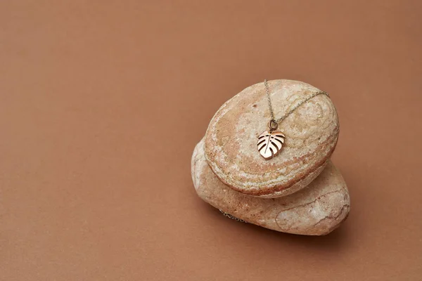 Elegante cadena de oro y colgante en forma de hoja de monstera sobre rocas sobre fondo beige —  Fotos de Stock