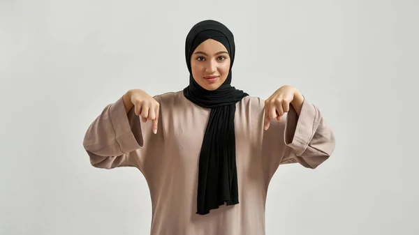 Щаслива молода арабська жінка в хіджабі вказуючи пальці вниз — стокове фото